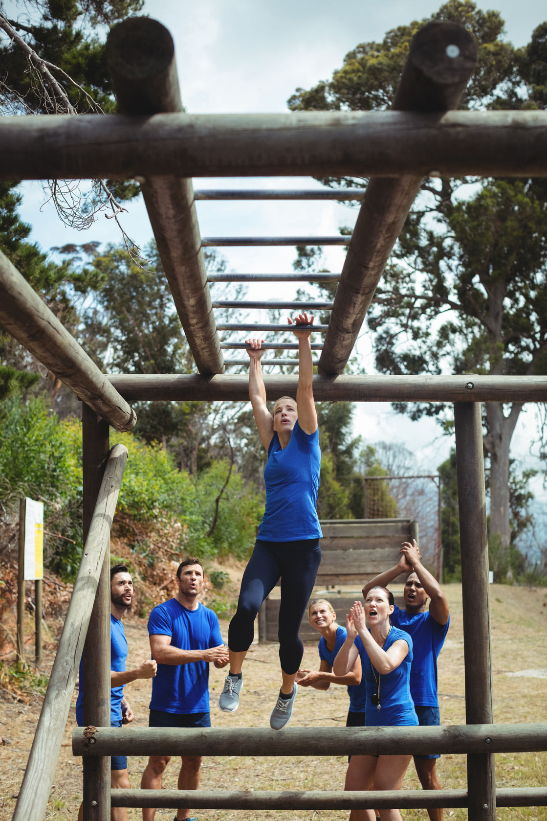 74454829 - fit woman climbing monkey bars while fit people cheering in background